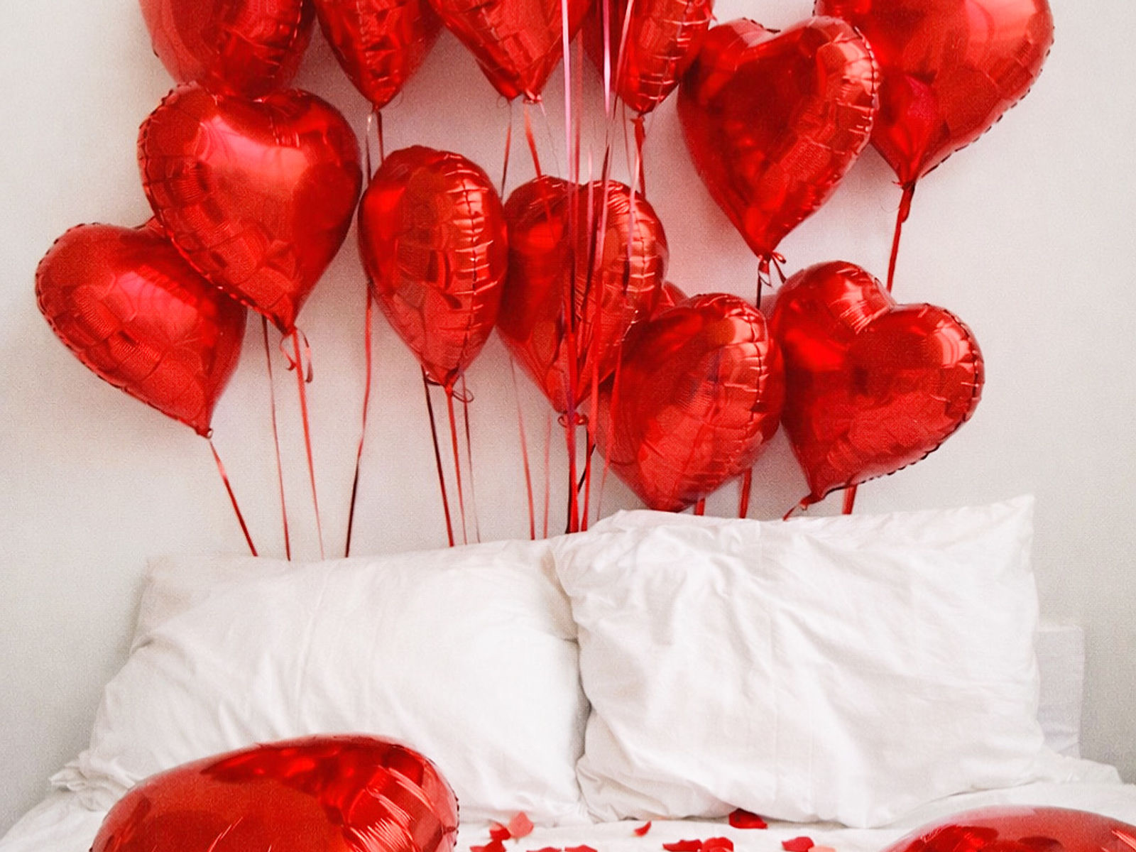 Red heart balloons above a romantic bed